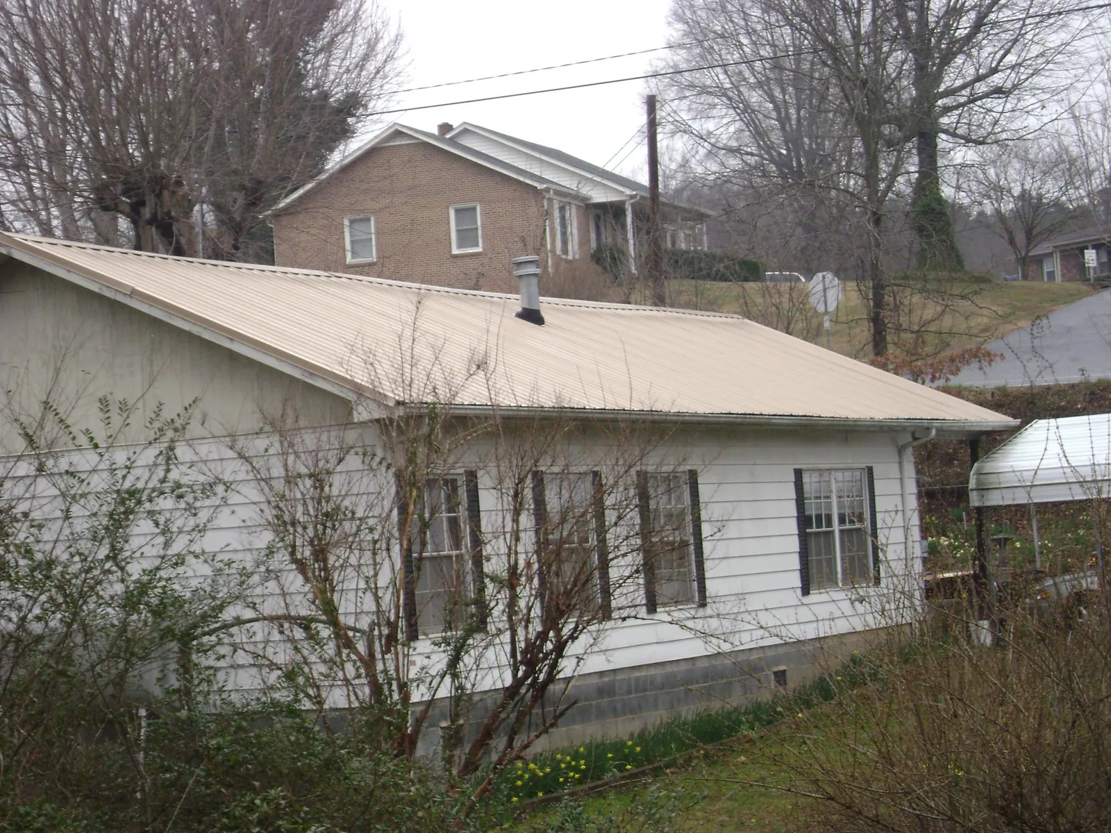 Tan metal roof on a white sided house set into a hillside — Commercial Roofing by Roofing Brothers in Rochester